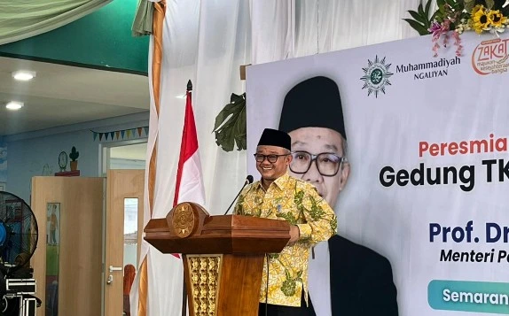Foto Menteri Pendidikan Dasar dan Menengah Abdul Mu'ti berpidato di podium peresmian gedung TK Muhammadiyah Ngaliyan, Semarang. Beliau tersenyum mengenakan kemeja batik dan peci hitam, berdiri di depan spanduk acara yang menampilkan wajahnya dan teks peresmian.
