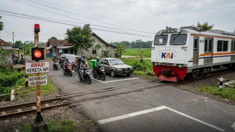 Pengendara mobil dan sepeda motor tertib berhenti di belakang garis aman pada perlintasan sebidang tanpa palang pintu saat kereta api KAI melintas, sebagai ilustrasi waspada kecelakaan kereta api Jawa Tengah.