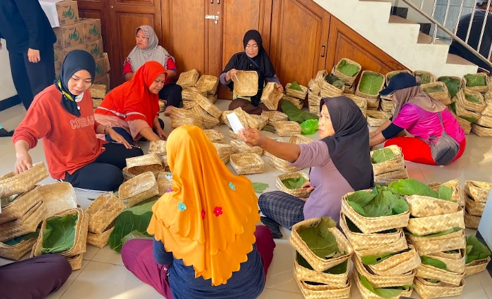 Sekelompok relawan perempuan di Semarang sedang menata daun jati segar ke dalam besek bambu sebagai wadah ramah lingkungan. Ini merupakan penerapan cara menyimpan daging kurban agar awet dan higienis tanpa menggunakan plastik hitam beracun.