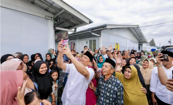 Gubernur Jateng Ahmad Luthfi memegang ponsel untuk berswafoto bersama kerumunan warga korban tanah gerak Tegal yang tersenyum ceria di area Hunian Sementara (Huntara) pada momen Iduladha 2026.