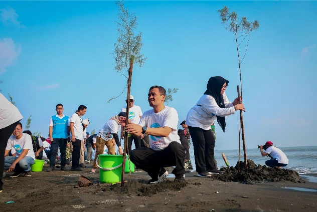Gubernur Jawa Tengah Ahmad Luthfi berjongkok di pasir pantai sambil memegang dan menanam bibit pohon cemara laut di Pantai Tirang Semarang.