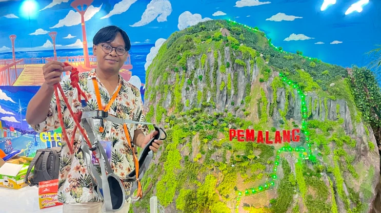 Ardian, pemandu Jimat Via Ferrata, menunjukkan perlengkapan keamanan tali karmantel dan harness untuk wisata ekstrem Jawa Tengah di depan maket tebing Bukit Jimat Pemalang.