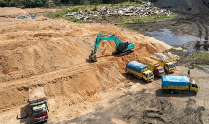 Ekskavator memuat tumpukan serbuk gergaji ke dalam armada truk sebagai bagian dari proses pengolahan limbah kayu untuk bahan bakar biomassa PLTU Adipala di Cilacap.
