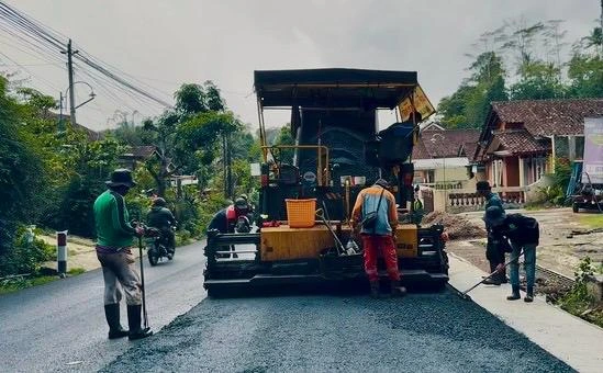 Alat berat paver aspal kuning sedang menggelar aspal hitam di jalan rusak Jateng, menunjukkan aksi perbaikan jalan Jawa Tengah di daerah pedesaan.