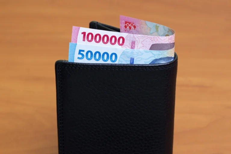 Uang Rupiah pecahan 100 ribu dan 50 ribu di dalam dompet kulit hitam, ilustrasi pencairan gaji ke-13 pensiunan tanpa potongan.