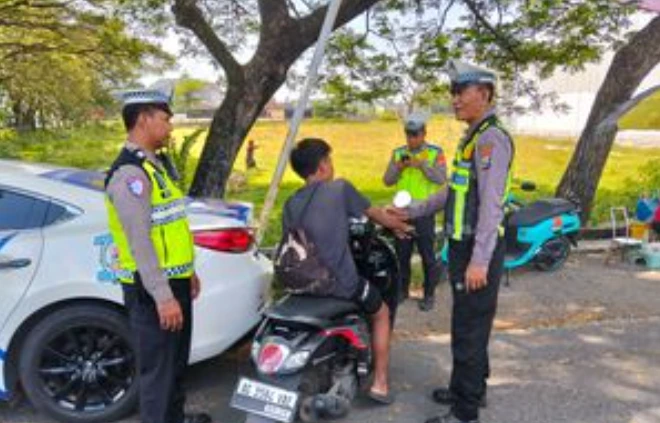 Empat petugas polisi lalu lintas Jateng berinteraksi dengan ramah kepada seorang pemuda pengendara sepeda motor skuter matik AG 3390 VBV di pinggir jalan raya, dekat mobil patroli, di bawah pohon besar. Salah satu petugas berbicara sambil tersenyum.