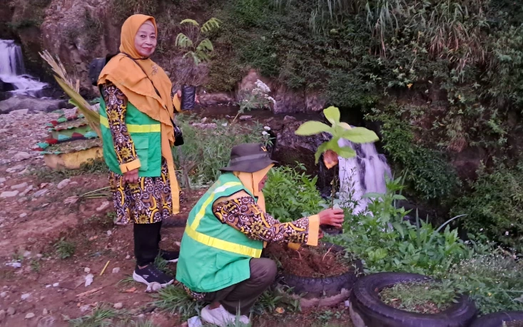 Dua relawan perempuan Aisyiyah Jateng mengenakan rompi hijau sedang melakukan aksi penanaman pohon di tepi aliran air terjun Jumog Putri, Tawangmangu, guna menghadapi perubahan iklim.