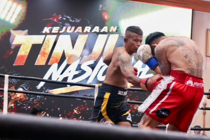 Dua atlet tinju bertato saling berbalas pukulan sengit di atas ring dengan latar belakang layar bertuliskan Kejuaraan Tinju Nasional dalam ajang Kejurnas Tinju Solo.