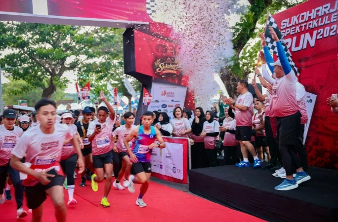 Ribuan pelari memulai perlombaan lari di bawah gerbang start merah besar dengan tulisan Sukoharjo Spektakuler Run 2026, dengan konfeti berterbangan dan bendera finish dikibarkan.