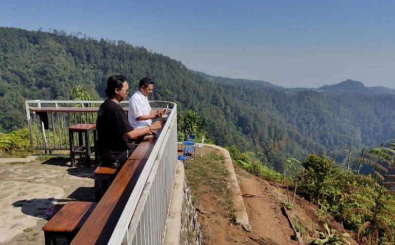 Dua pengunjung pria menikmati panorama lembah hutan pinus dari balkon kayu Kopi Sedawung, destinasi hidden gem Batang.