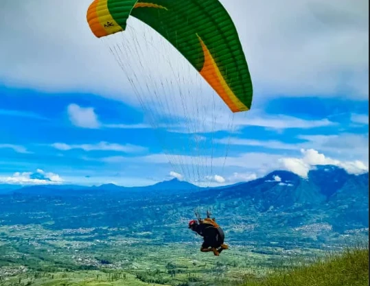 Wisatawan menikmati olahraga ekstrem paralayang di Bukit Kekeb, wisata Wonosobo terbaru dengan pemandangan alam pegunungan hijau dan langit biru.