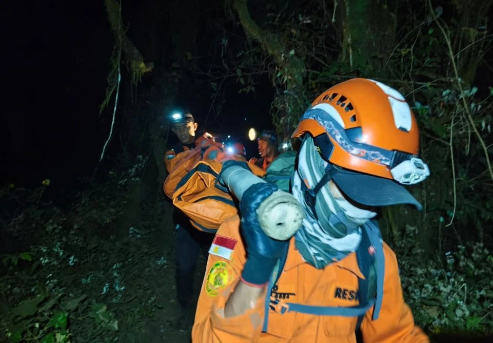Tim SAR gabungan mengenakan seragam oranye dan headlamp sedang menandu korban evakuasi pendaki jatuh di Gunung Slamet menyusuri jalur hutan pada malam hari.