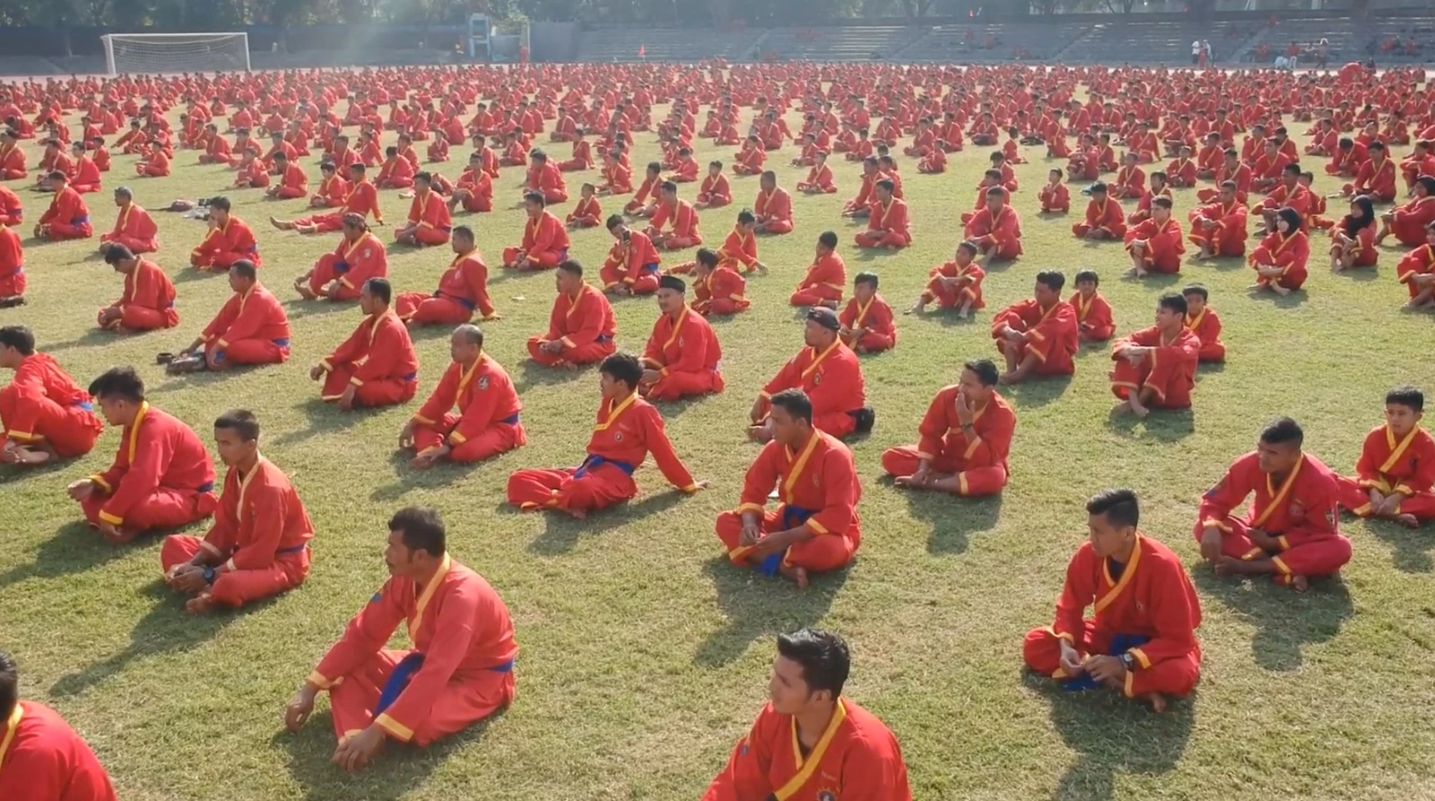 Ilustrasi ribuan pesilat Tapak Suci Putera Muhammadiyah berseragam merah duduk bersila dengan rapi di sebuah lapangan rumput terbuka saat mengikuti kegiatan apel massal.