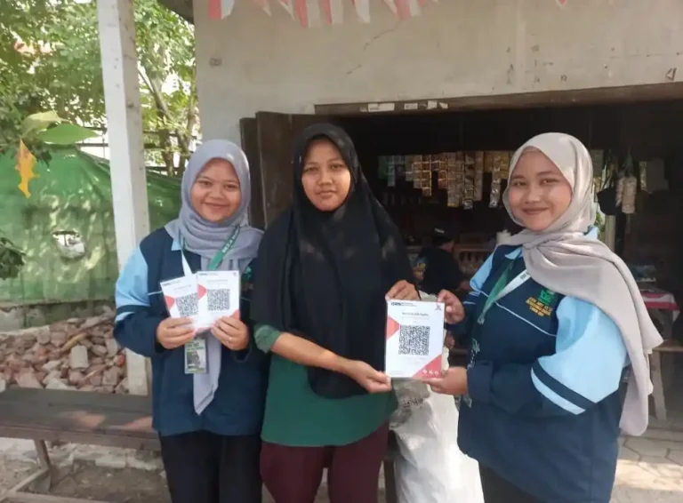 Dua mahasiswa KKN UIN Walisongo Semarang mendampingi pelaku UMKM memegang cetakan barcode QRIS untuk warung kecil di Desa Putatgede Kendal.