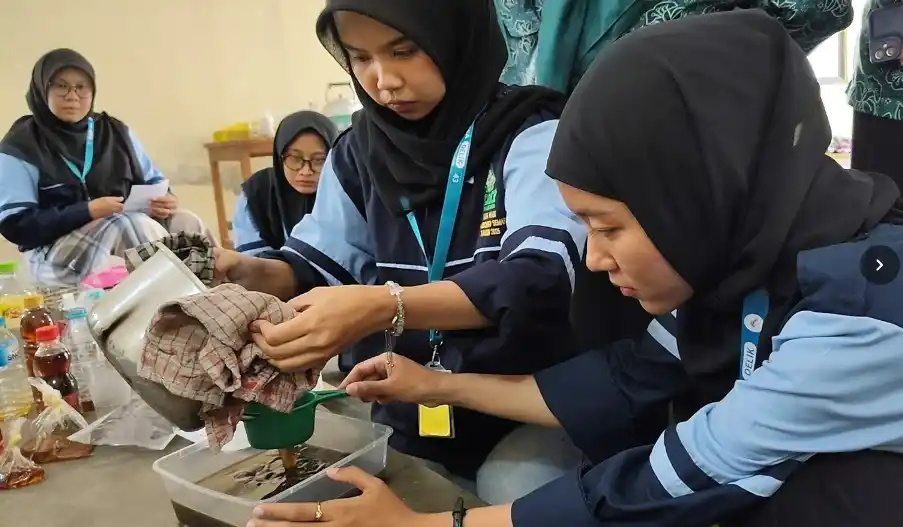 Dua mahasiswi KKN UIN Walisongo sedang menyaring limbah minyak jelantah kotor menggunakan saringan hijau ke dalam wadah plastik sebagai persiapan bahan baku peluang usaha lilin aromaterapi.