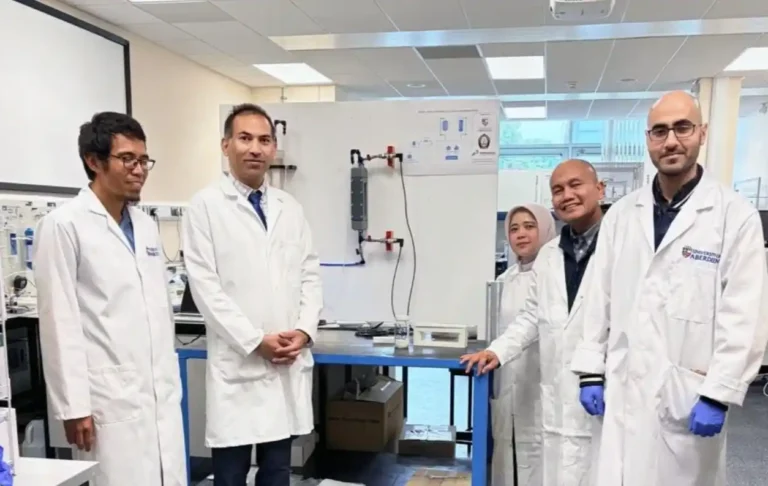 Lima peneliti Undip dan University of Aberdeen berjas lab berdiri di sekitar peralatan riset teknologi membran untuk pemulihan lithium. Papan tulis menampilkan diagram teknis di School of Engineering, University of Aberdeen.