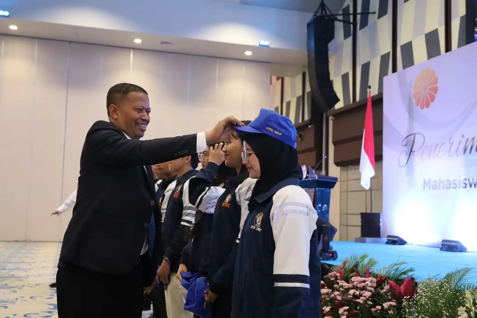 Rektor Undip Prof Suharnomo tersenyum hangat saat melepaskan topi secara simbolis dari perwakilan mahasiswa KKN Undip yang berdiri berjajar dalam acara Gelar Karya di Muladi Dome Semarang.
