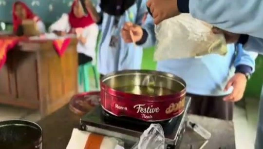 Mahasiswa KKN MIT memandu proses pencampuran bahan baku ke dalam wadah berisi minyak jelantah panas di atas kompor portabel untuk diolah menjadi lilin aroma terapi.