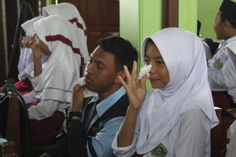 Seorang siswi sekolah dasar berhijab putih menyeka air mata dengan tisu di sebelah mahasiswa KKN saat meresapi materi edukasi anti bullying di dalam ruang kelas.