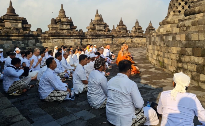 Sekelompok umat Buddha dan peserta berpakaian putih duduk bermeditasi dalam posisi peribadatan di pelataran Candi Borobudur saat pagi hari, dengan latar belakang stupa-stupa candi.