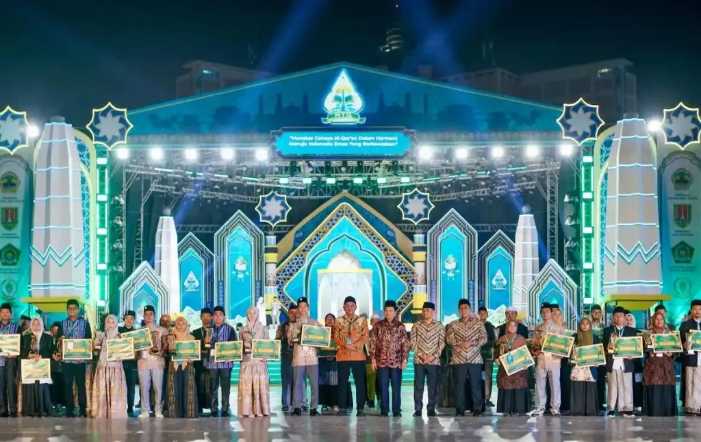 Puluhan pemenang berfoto bersama jajaran pejabat dan dewan hakim sambil memegang piagam penghargaan pada malam pengumuman Daftar Lengkap Juara MTQ Nasional 2026 di panggung utama Simpang Lima, Semarang.