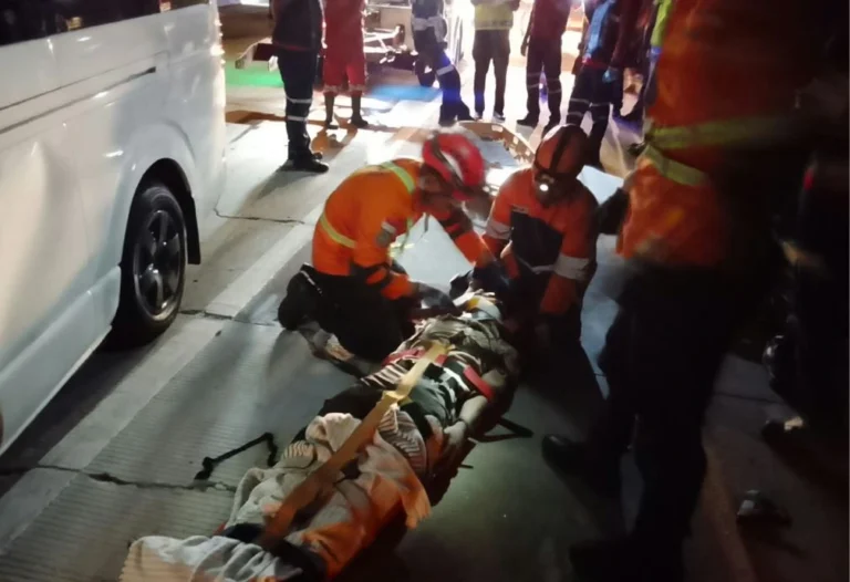 Petugas Basarnas dengan seragam oranye sedang mengikat korban kecelakaan di Tol Pemalang ke tandu basket pada malam hari.