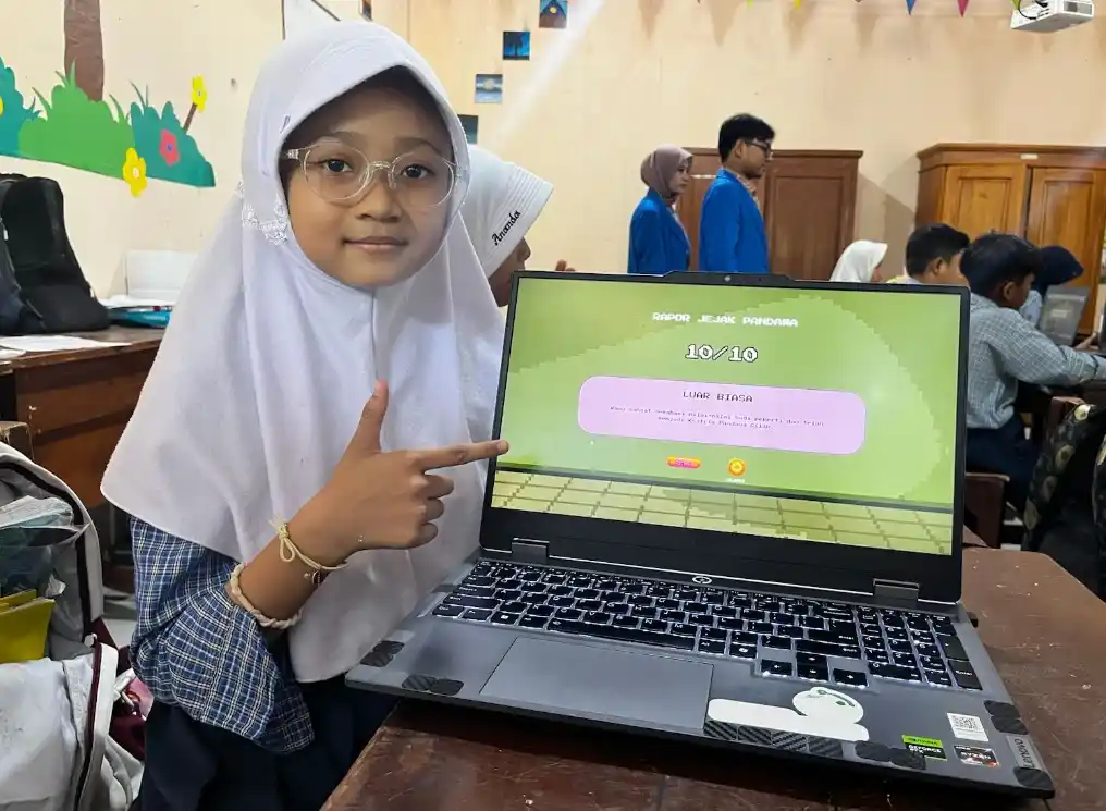 Siswi SD Negeri Kalibanteng Kulon 01 Semarang tersenyum sambil menunjuk layar laptop yang menampilkan rapor nilai sempurna setelah menyelesaikan level game edukasi wayang.