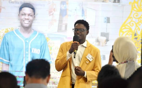 Joseph Mamvura, mahasiswa internasional Unsoed asal Zimbabwe, berbicara menggunakan mikrofon mengenakan jaket almamater kuning di hadapan peserta orientasi SISO 2026.