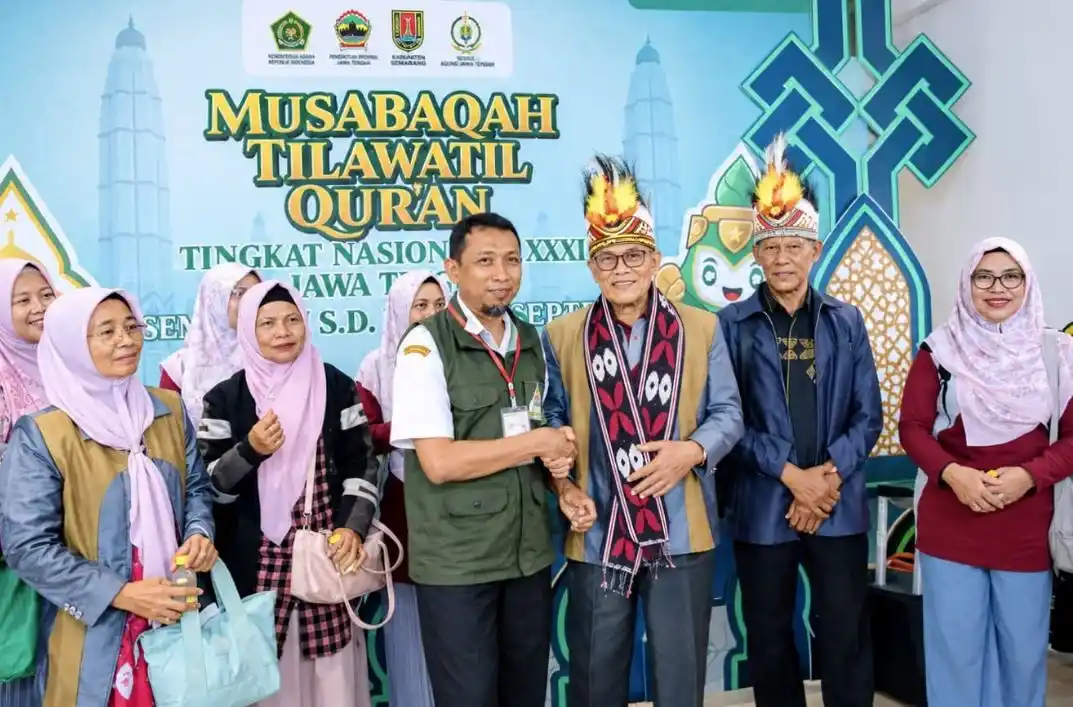 Panitia MTQ Nasional 2026 Jawa Tengah berjabat tangan menyambut perwakilan Kafilah Papua Barat Daya yang mengenakan mahkota khas Papua dan selendang rajut Jepara berlatar belakang backdrop resmi MTQ.