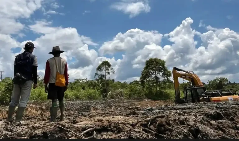 Dua orang pria memantau alat berat ekskavator yang sedang menggali tanah berlumpur untuk pembangunan embung irigasi di Kampung Woslay, Keerom, Papua guna mengatasi kekeringan pertanian.