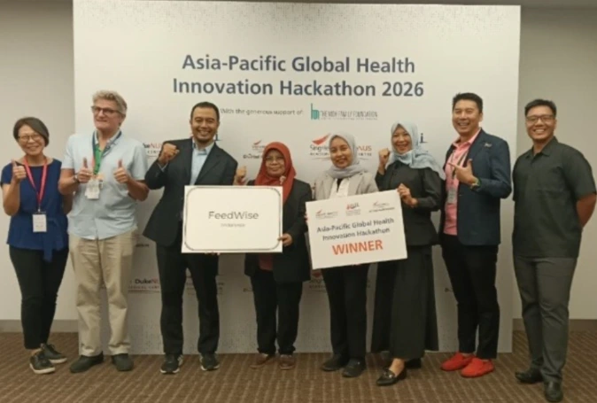 Sekelompok delapan orang berpose di depan latar belakang acara resmi dengan tulisan 'Asia-Pacific Global Health Innovation Hackathon 2026'. Dua orang di tengah memegang papan besar. Papan kiri bertuliskan 'FeedWise' dan papan kanan bertuliskan 'Asia-Pacific Global Health Innovation Hackathon WINNER'. Terdapat logo SingHealth Duke-NUS Global Health Institute.