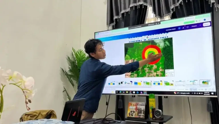 Seorang mahasiswa dari Tim 17 Ekspedisi Patriot UNDIP mempresentasikan data survei pemetaan lokasi Embung Senggi menggunakan peta satelit dan overlay radar pada layar televisi besar.